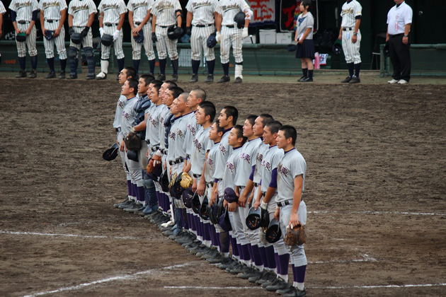 校旗が掲揚され,校歌を歌う選手たち